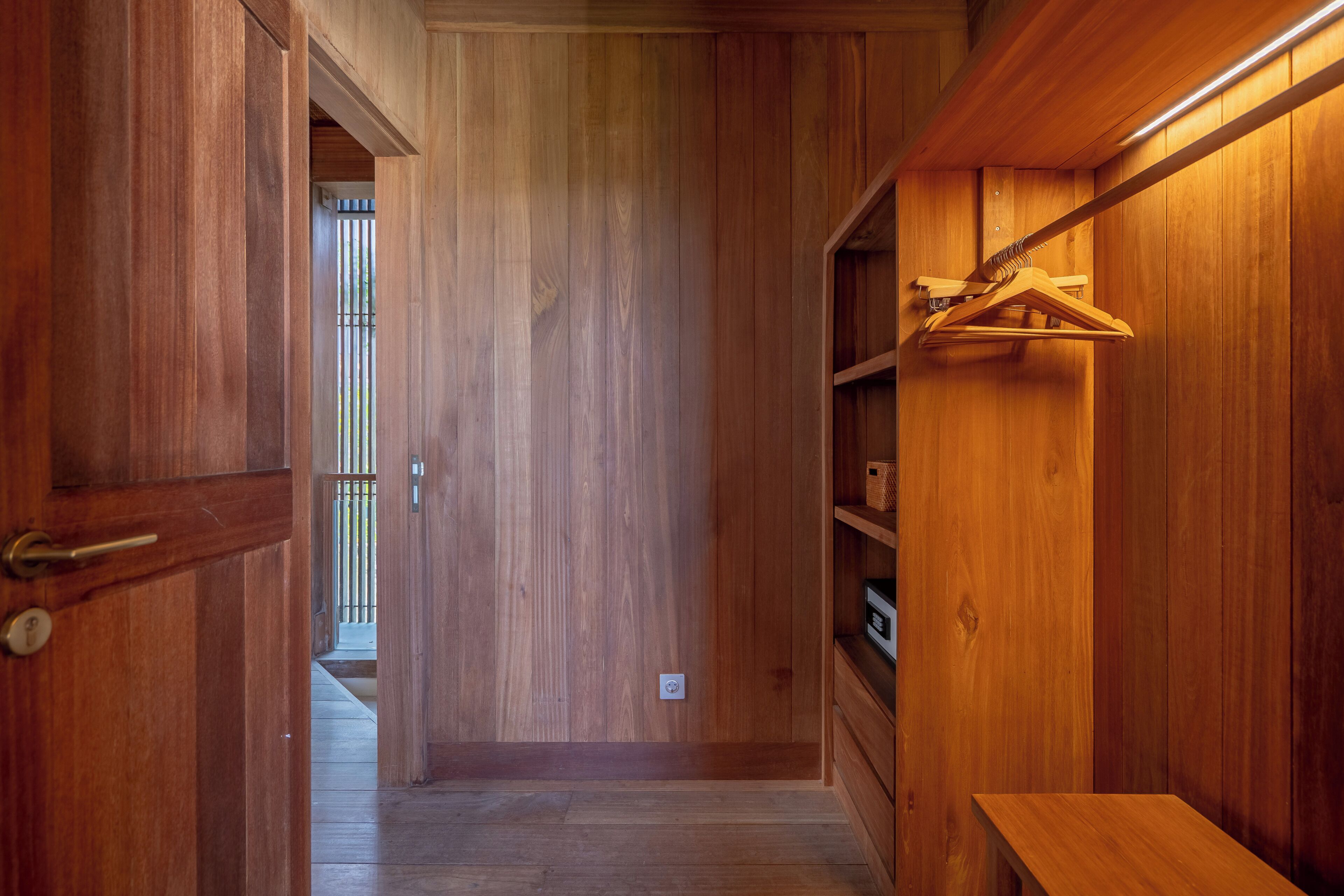 Un intérieur en bois, avec une porte en bois, un banc et un porte-manteau suspendu.