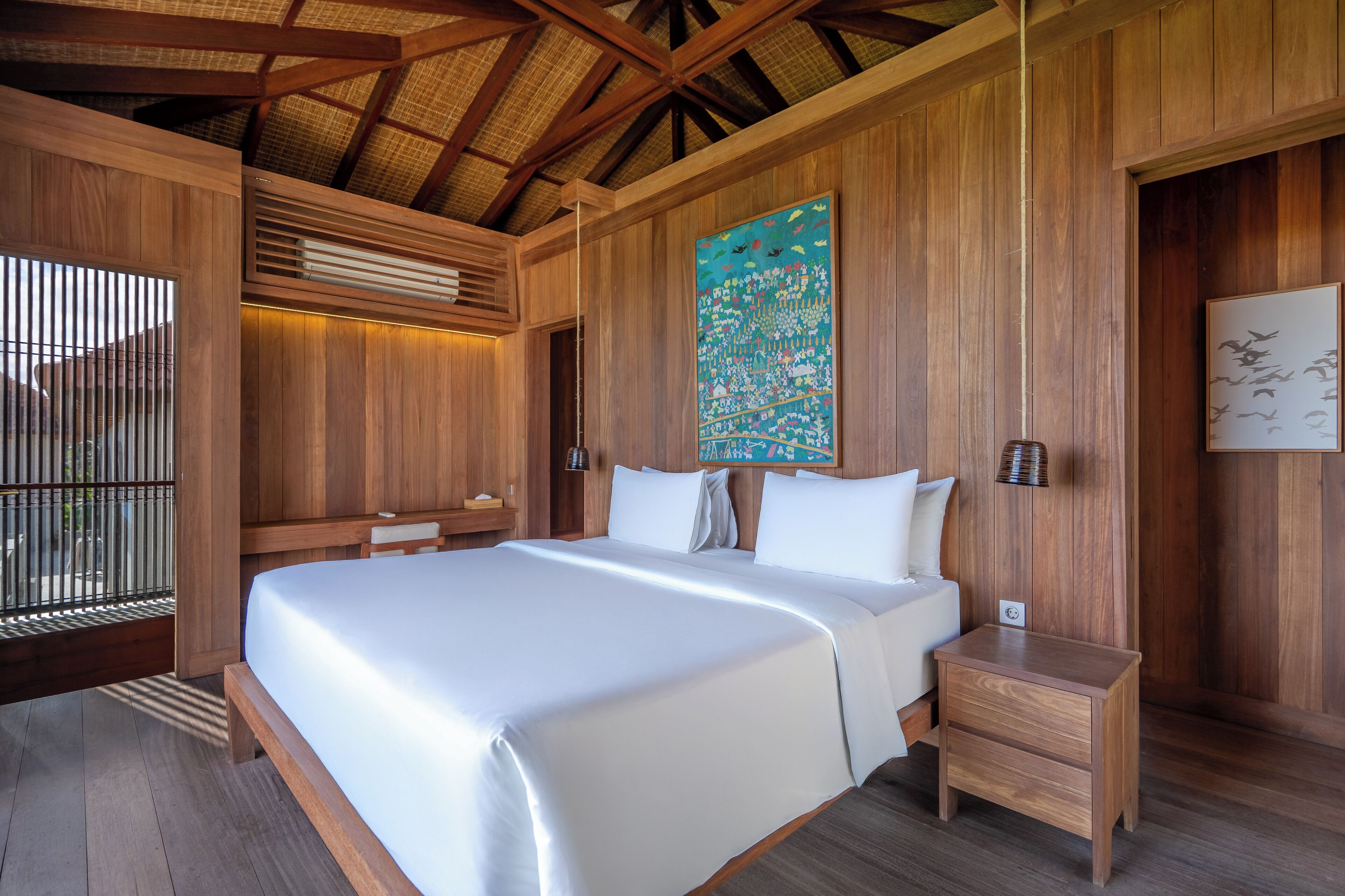A wooden room with a bed, bedside tables, and a large painting on the wall.