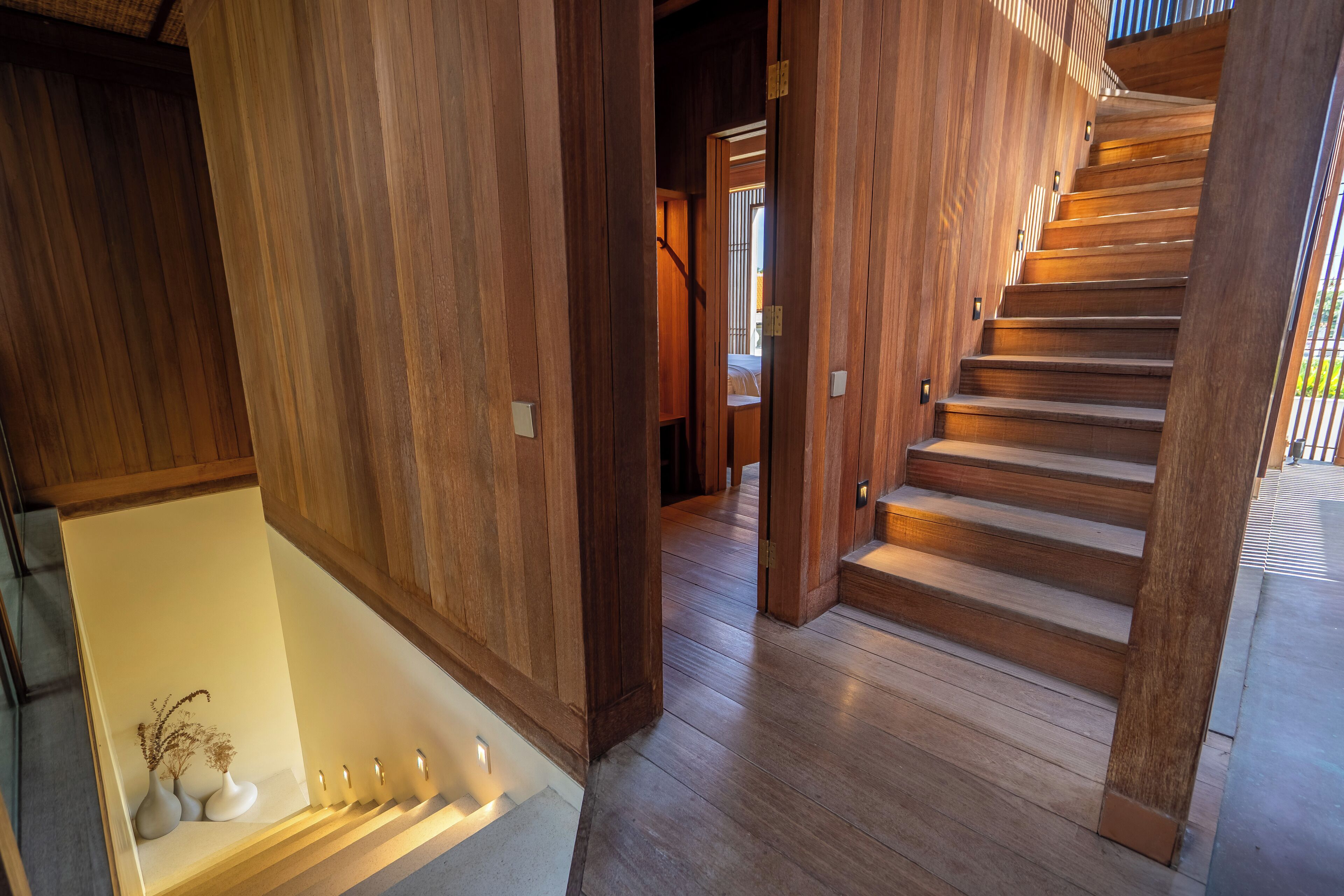 A wooden staircase with a handrail, leading to a second-floor landing with a light fixture and a small table with vases.