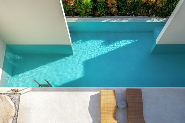 A clear blue pool with a lounge area and a view of greenery.