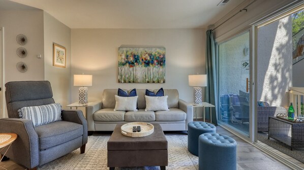 A living room with a grey sofa, a grey armchair, a coffee table, and a glass door leading to an outdoor area.