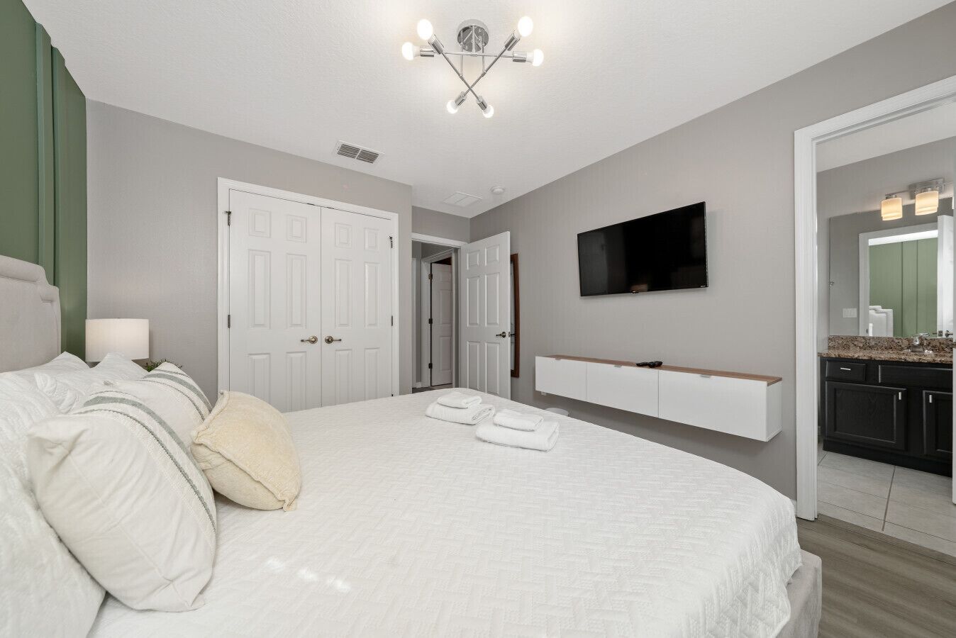 A bedroom with a large bed, a TV mounted on the wall, and a bathroom visible through an open door.
