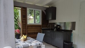 Eine kleine Küche mit Essbereich, mit einem Tisch, dessen Tischdecke ein Kaffeemotiv zeigt, einer Spüle und einem Fenster mit Blick auf einen Garten.