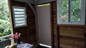 Ein Zimmer mit Holzeinrichtung, einem Tisch mit gemustertem Tischläufer, einer Vase mit Blumen und einem Fenster mit Jalousien.
