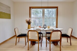 Een eetgedeelte met een ronde tafel voor vier personen, omringd door houten stoelen met gevlochten rugleuningen. Achter de tafel bevindt zich een raam met uitzicht op bomen.