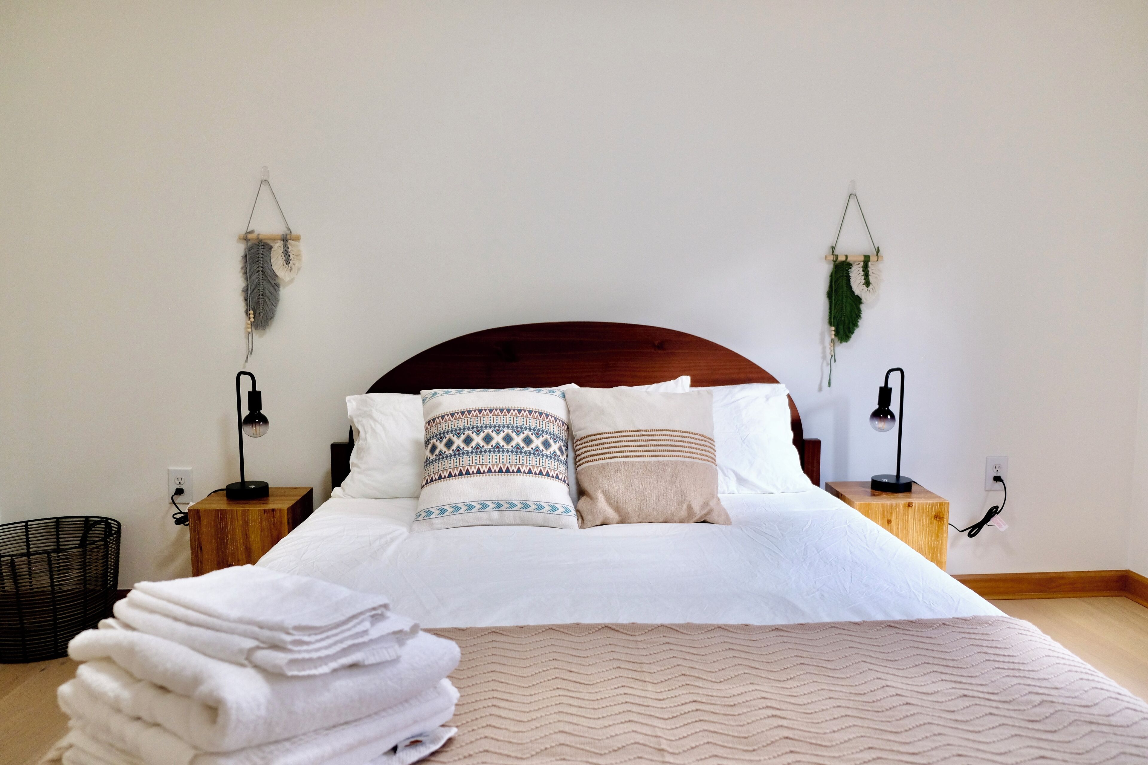 Een keurig opgemaakt bed met gestreepte kussens, een bedlampje en een aan de muur bevestigde plant.
