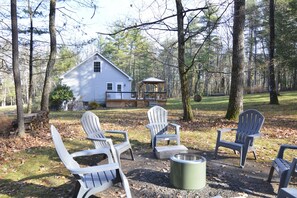 Een rustieke blokhut met Adirondack-stoelen en een vuurkuil in een bebost gebied.