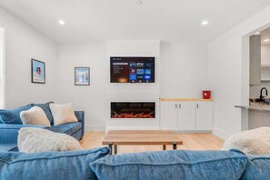 A modern living room with a sofa, a fireplace, a mounted TV, and a wooden table.
