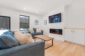A modern living room with a sofa, a coffee table, a fireplace, and a mounted TV displaying streaming services.