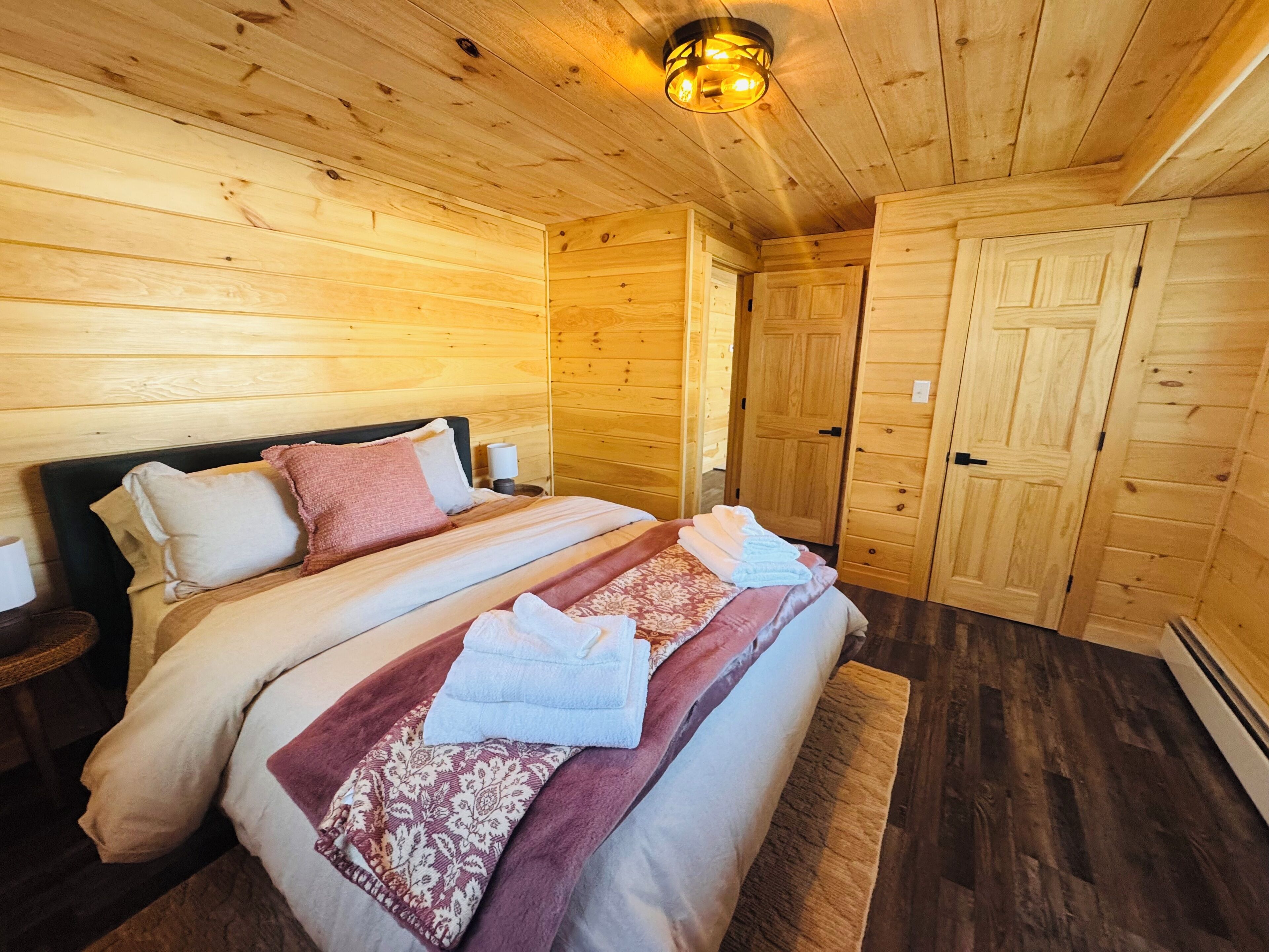 A wooden cabin bedroom with two beds, a nightstand, and a door.