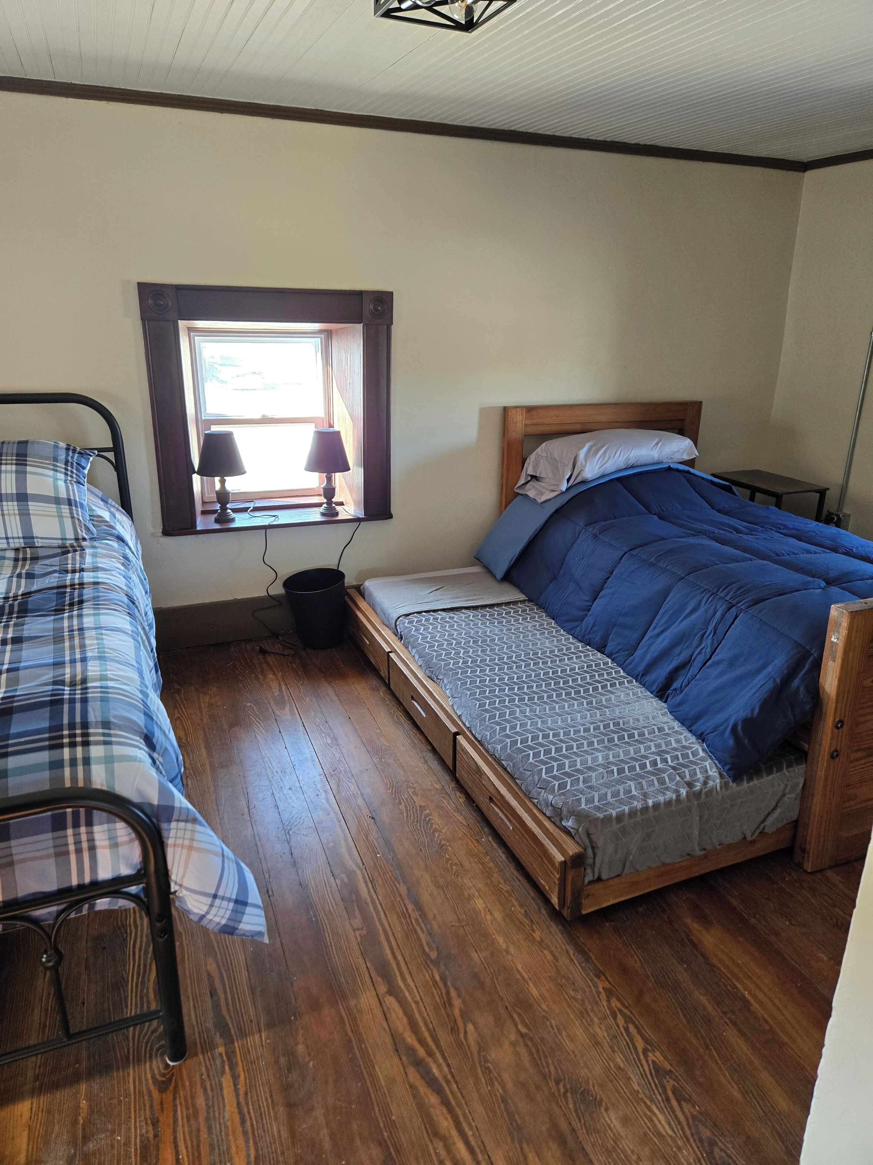 Un dormitorio con una cama de madera, una cama individual, una ventana con lámpara y suelo de madera.