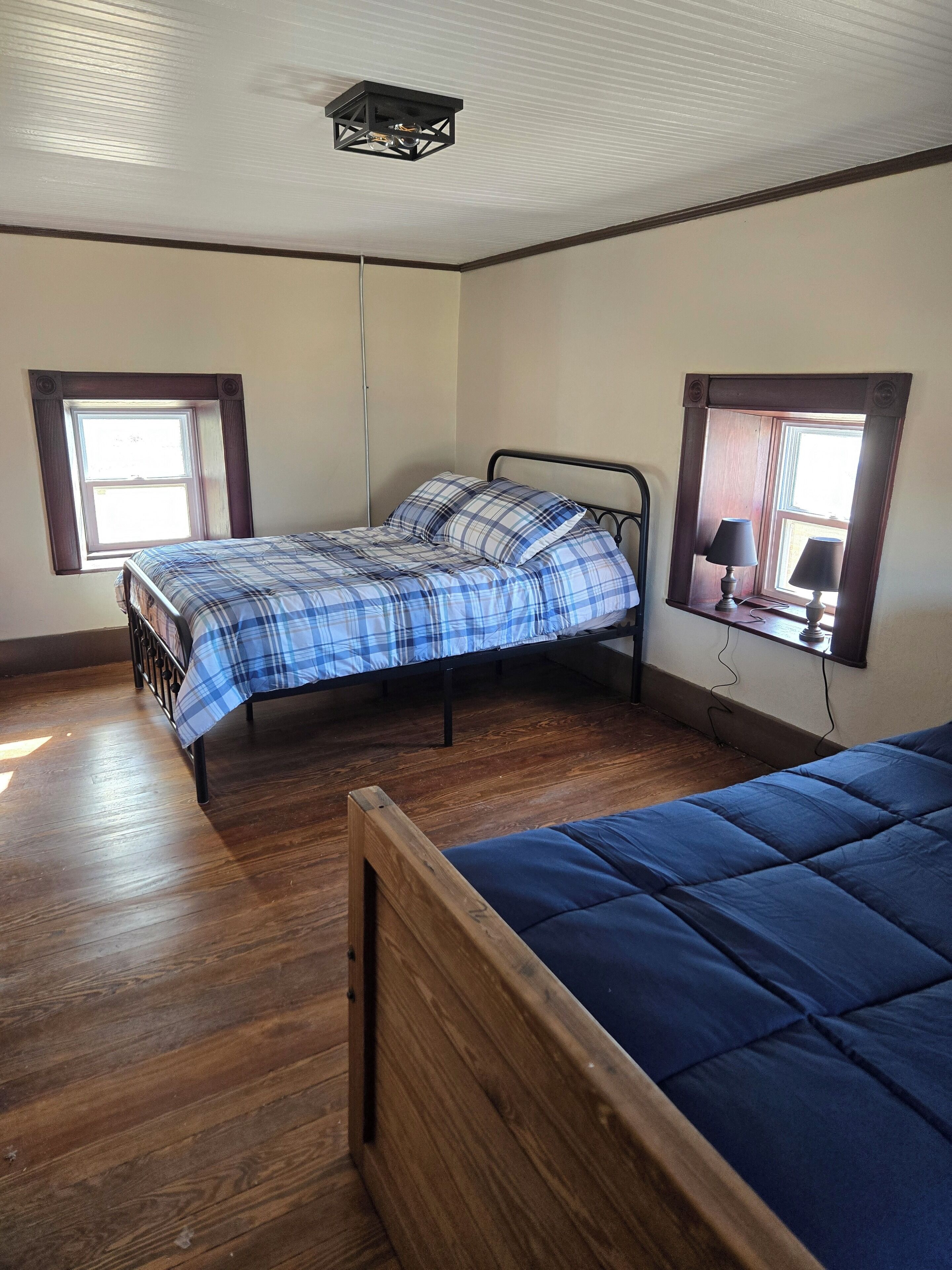 Una camera da letto con un letto in legno, un letto più piccolo con materasso blu, una finestra con una lampada e un lampadario.