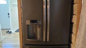 Un refrigerador de acero inoxidable con dispensador de agua, ubicado en una habitación con paredes de piedra y suelo de madera.