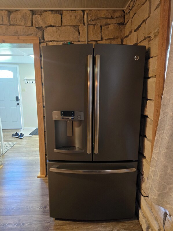 A stainless steel refrigerator with a water dispenser, located in a room with stone walls and wooden flooring. - Das Stein Haus! Charming 2-bedroom limestone house in Liebenthal, Kansas. (Liebenthal)
