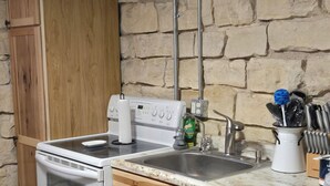 Una cocina con estufa blanca, armarios de madera, encimera de granito y pared de piedra.