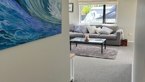 A modern living room with a grey sofa, a coffee table, and a large wave painting on the wall.