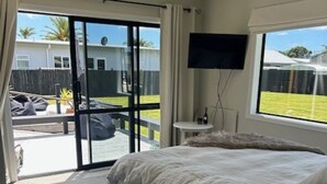 A bedroom with a large bed, a TV mounted on the wall, and a sliding glass door leading to an outdoor area.
