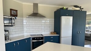 A kitchen with white tiled backsplash, blue cabinets, a stainless steel range hood, a microwave, and a refrigerator.
