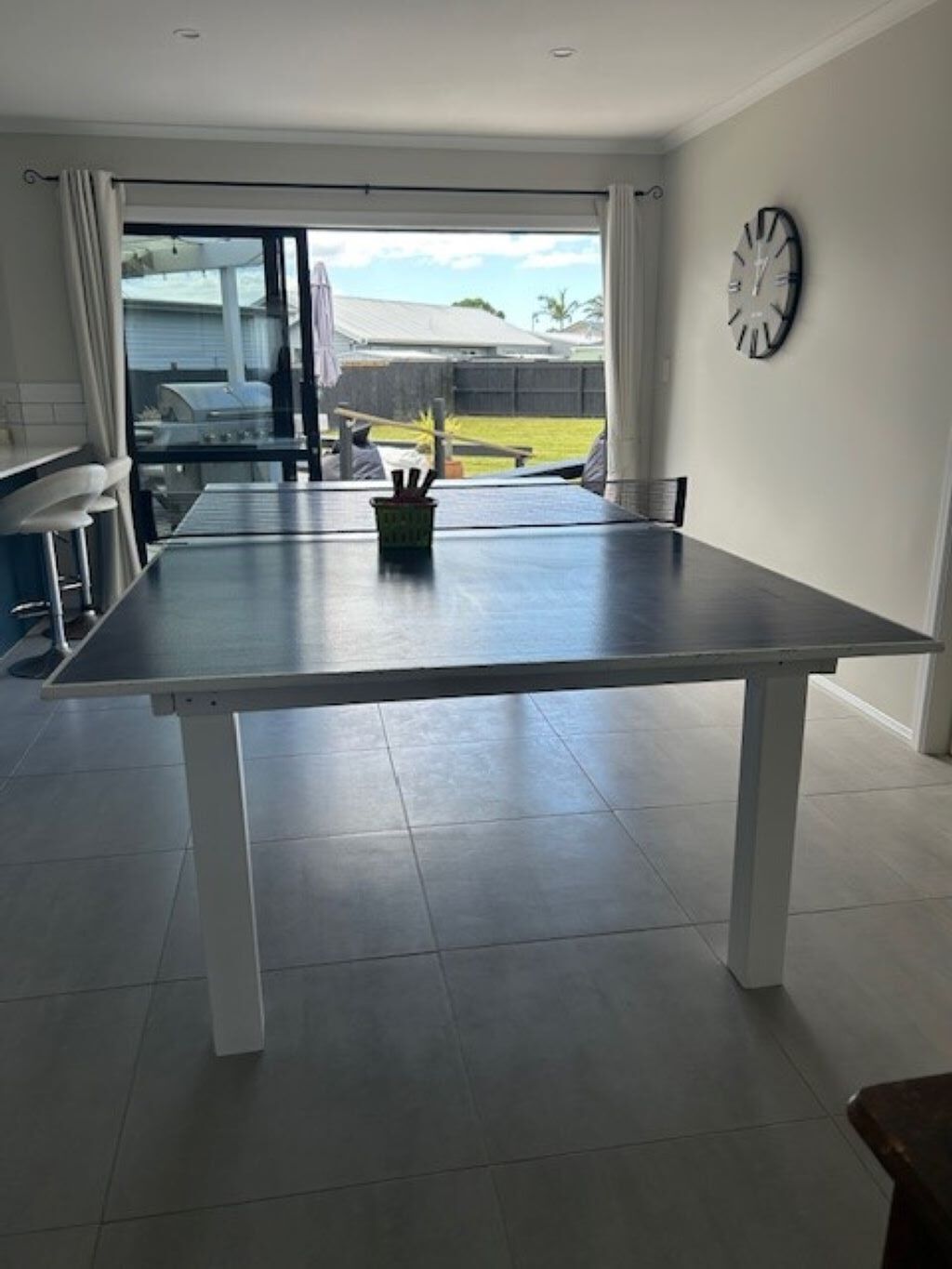 Una cocina moderna con una mesa grande, un reloj en la pared y vista al jardín trasero.
