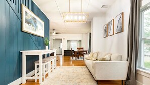 Un salon moderne avec un canapé blanc, une table à manger avec des chaises, un banc et une grande fenêtre avec des rideaux.