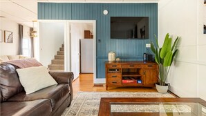 Un salon avec un canapé en cuir marron, une table basse en bois, un mur d’accent bleu, une grande plante et un meuble en bois sur lequel est posée une télévision.