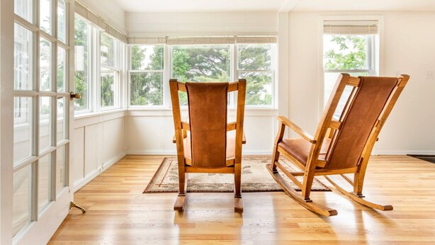 Une pièce dotée de deux fauteuils à bascule, de grandes fenêtres et d’un plancher en bois.