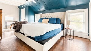 Une chambre à coucher avec un lit, un ventilateur de plafond, une fenêtre avec des stores et une petite table avec une lampe.