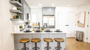 A modern kitchen with a central island, four bar stools, and built-in shelves. - Waterfront Golf Retreat | Balcony Views | Saddlebrook Resort Amenities (Wesley Chapel)