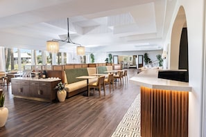 A spacious hotel lobby with a reception desk, seating area, and large windows offering views of the outdoors.