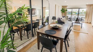 A modern dining area with a large table, chairs, and a bowl of fruit. There are potted plants and a view of the outdoors through large windows. - Waterfront Golf Retreat | Balcony Views | Saddlebrook Resort Amenities (Wesley Chapel)