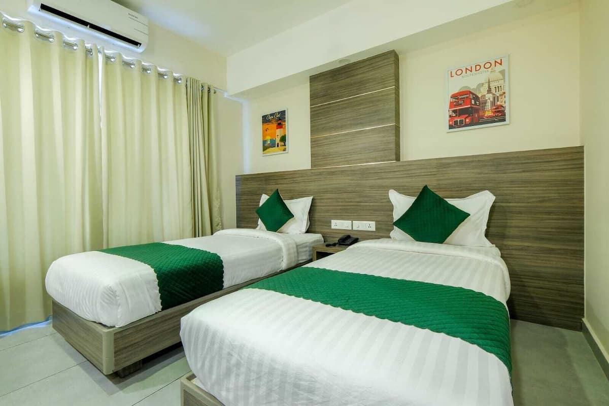 A hotel room with two beds, each with a green and white bedspread, a wooden headboard, and a poster of London on the wall.