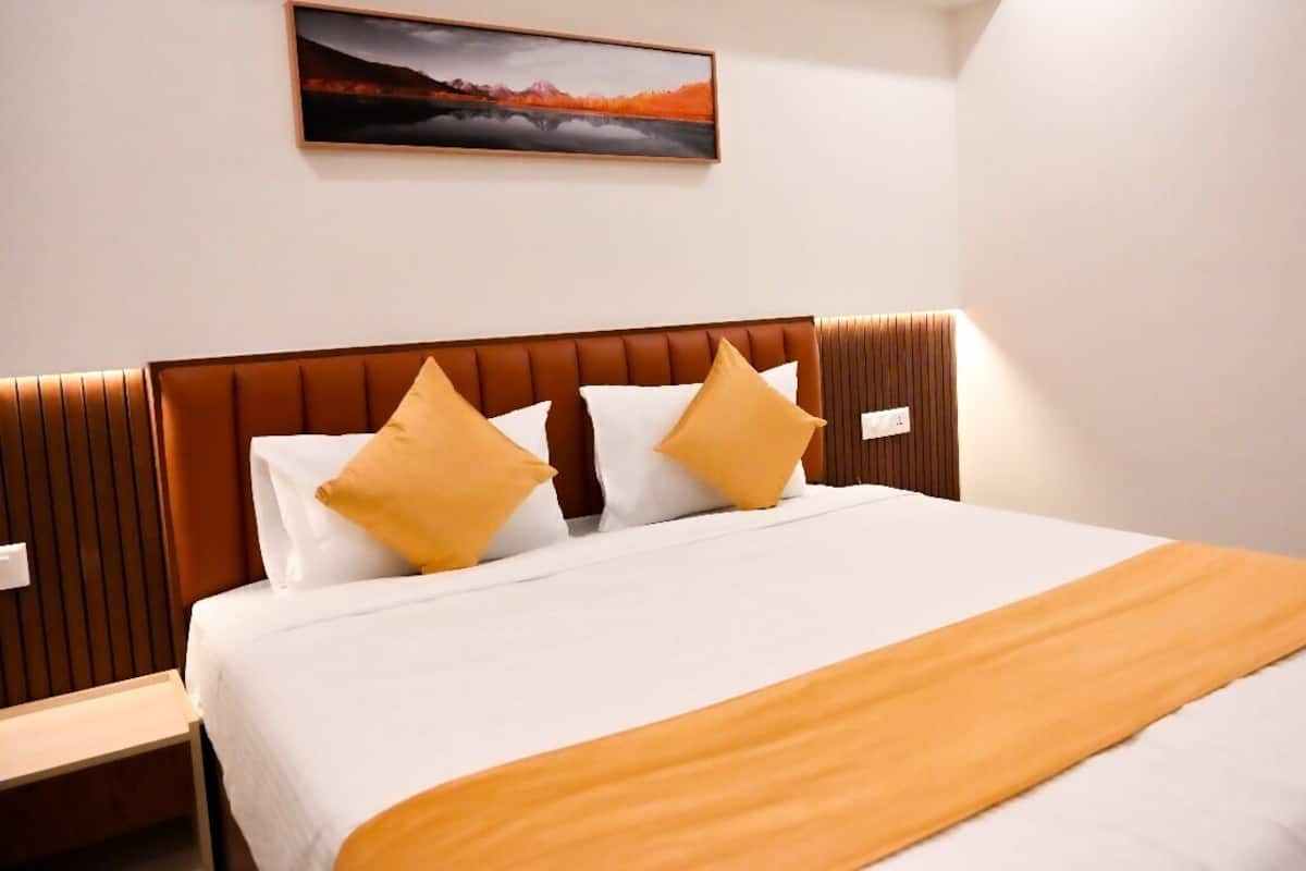 A neatly made bed with white and yellow bedding, a brown headboard, and a painting above it.