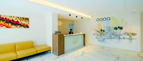 A modern reception area with a marble floor, a yellow sofa, a wooden reception desk, and a colorful abstract painting.