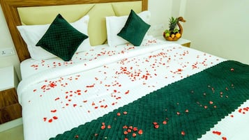 Una cama con colcha verde y blanca a rayas, dos almohadas verdes y pétalos de rosa roja esparcidos sobre la cama.