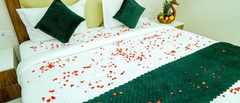 A bed with a white and green striped bedspread, two green pillows, and red rose petals scattered across the bed.