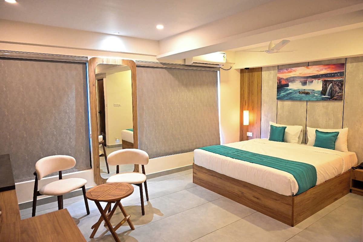 A modern hotel room with a large bed, a seating area with chairs, and a painting on the wall.