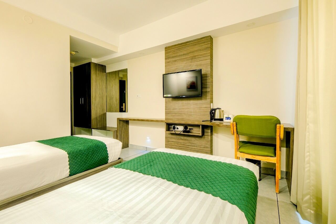 Ein Hotelzimmer mit zwei Betten, einem an der Wand befestigten Fernseher, einem Schreibtisch mit Stuhl und einem Spiegel.