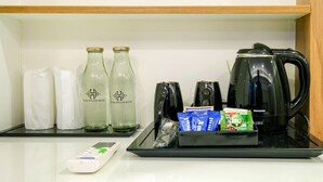 A hotel minibar setup with two glass bottles, a black electric kettle, a remote control, and some packaged snacks. - The Heartland Business Hotel (Thiruvananthapuram)