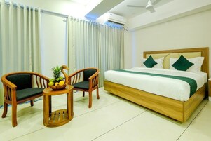 A bedroom with a wooden bed, two wooden chairs, a small round table with a fruit bowl, and a window with curtains.