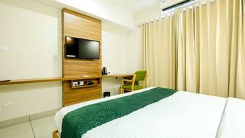 A hotel room with a bed, a TV mounted on a wooden panel, a chair, and a curtain.