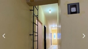 A corridor with a metal ladder on the left, a door at the end, and a framed item on the right wall. - CJ HOMESTAY (Batam)