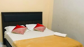 A bed with a black headboard, white bedding, and a mustard-colored blanket. - CJ HOMESTAY (Batam)