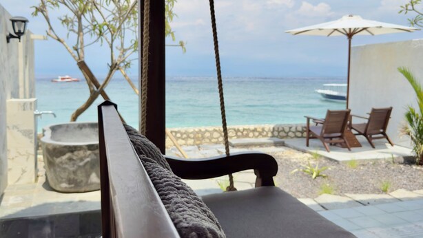 A beachside lounge with a swing chair, a stone basin, and a view of the ocean.