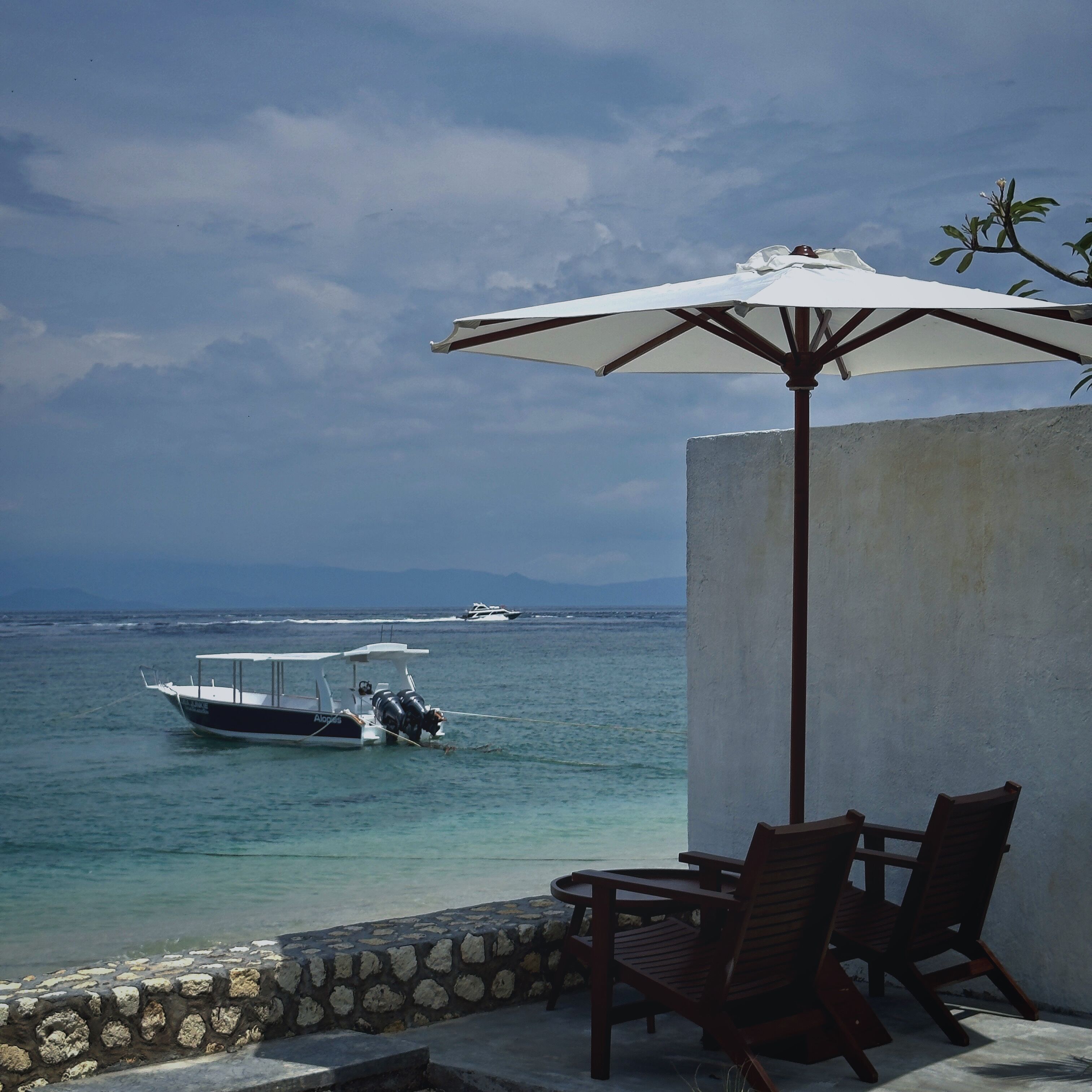 A seaside patio with a table and chairs, overlooking the sea.