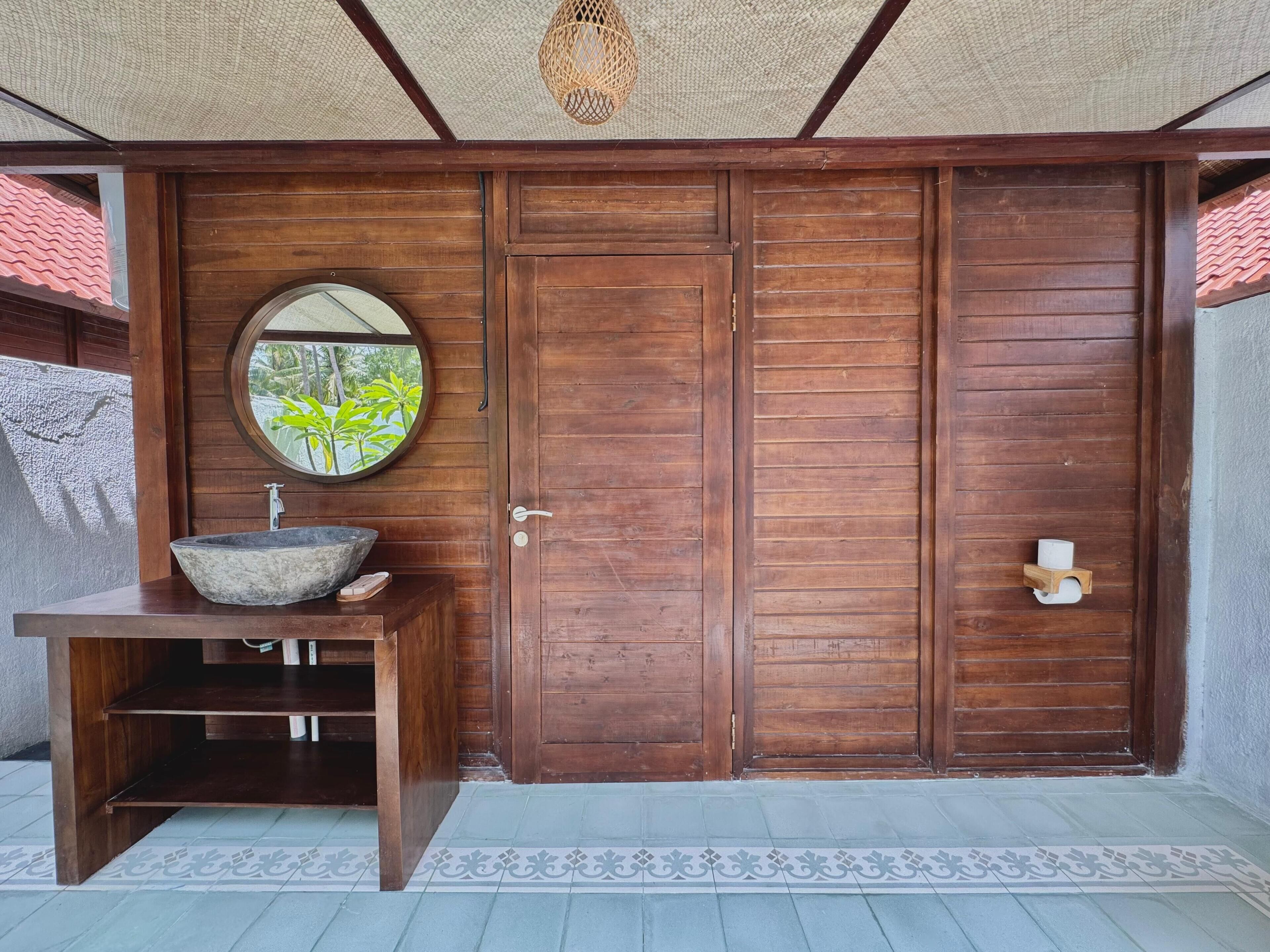 Une porte en bois ornée d’un miroir rond et d’un lavabo en pierre.