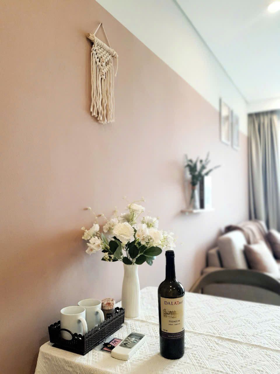 Una mesa con una botella de vino, un jarrón de flores y una bandeja con tazas y un control remoto.