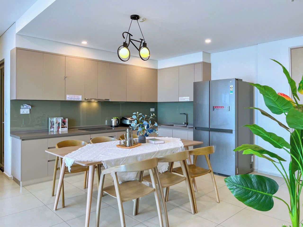 A modern kitchen with a dining area, featuring a table with chairs, a refrigerator, and a unique bicycle-shaped light fixture.
