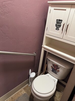 A bathroom with a white toilet, a trash bin, and a cabinet with a sign that says "Flush the toilet, Close the lid". - Delightful 3-bedroom COZY ROOMY  house  in Beautiful Powell WYOMING with WiFi ! (Powell)