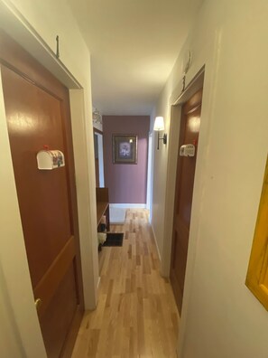 Un pasillo con puertas de madera, un buzón, un cuadro enmarcado en la pared y una lámpara.