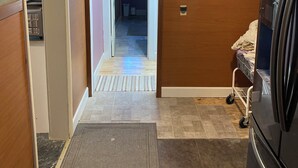 A hallway with a refrigerator, a door leading to a bathroom, and a mat at the entrance.